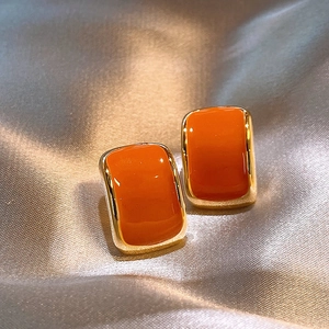 Detail of square orange enamel stud earrings with gold base on champagne silk
