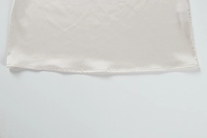 Macro detail of glossy satin fabric hem with precise stitching on an ivory cocktail dress