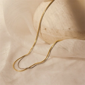 Detail of double-layer snake chain necklace in gold and silver finish on soft fabric