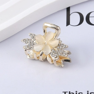 Macro detail of floral hair claw clip with white cat-eye petals and sparkly rhinestones