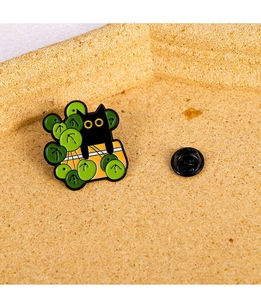 Macro shot of cartoon black cat in green plant enamel pin with secure rubber clutch back