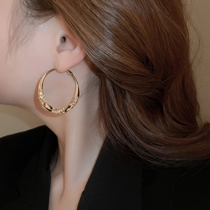 Close-up of golden twisted hoop earrings with textured lava finish on a female model