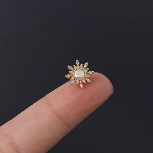 Detailed close-up of a tiny gold sunburst stud earring with white opal and zircon on a fingertip