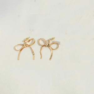 Macro shot of 14K gold plated bow earrings with metallic mesh texture on stone background