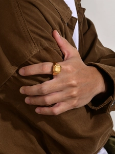 Close-up of men's gold geometric square ring worn with a brown utility jacket
