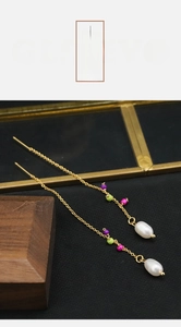 Detail of long gold drop earrings featuring colorful beads and baroque pearls on textured fabric