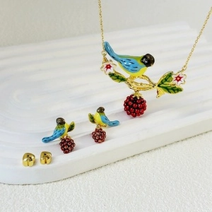 Detail of enamel bird jewelry set with floral patterns on white plaster tray