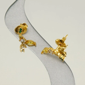 Detailed shot of golden banana-shaped earrings with colorful cubic zirconia on silk ribbon