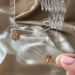 Close-up of golden hexagonal earrings with logo and crystals on acrylic hanger