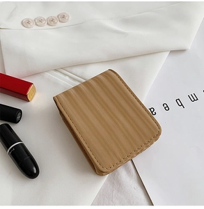 Close-up of khaki striped mini makeup pouch with mirror on a white blazer