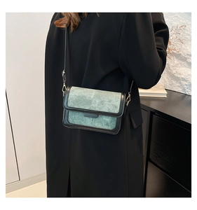 Side view of retro green and black crossbody bag worn by a model in a long black coat