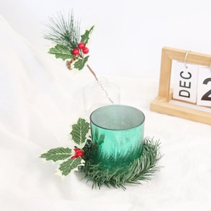 Detailed close-up of green glass candle holder with red berry and holly leaf wreath