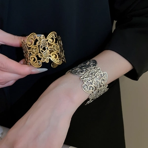 Detailed view of wide open cuff bracelets with intricate hollow floral patterns in gold and silver