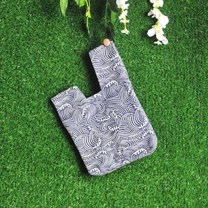Japanese knot wrist bag in blue fabric featuring traditional white wave patterns on green grass