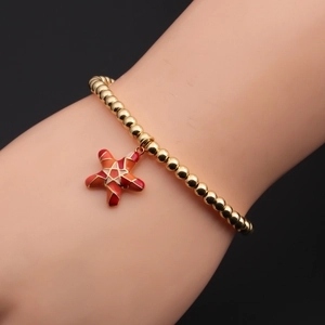 Detail eines goldenen Perlenarmbands mit rotem Emaille-Seestern-Anhänger am Handgelenk
