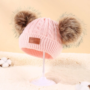 Pink cable knit beanie for kids featuring double brown pom-poms and a leather patch