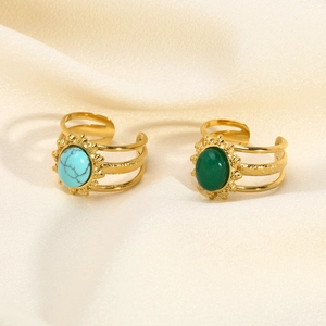 Close-up of gold layered rings with turquoise and green stones on beige fabric