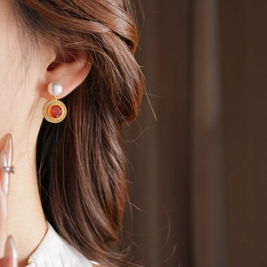 Détail d'une boucle d'oreille vintage dorée avec perle blanche et pierre orange