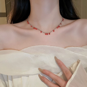 Gros plan d'un collier de perles argentées avec pendentifs gouttes rouges sur modèle