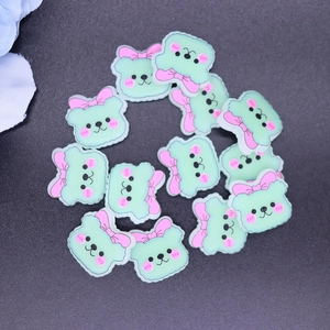 Close-up of mint green cartoon animal resin charms with pink bows for DIY crafts
