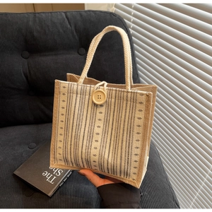 Detail of jute tote bag with beige striped panel, wood button and woven handles