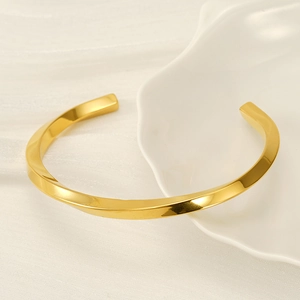 Minimalist twisted C-shape gold stainless steel cuff bracelet on ceramic display