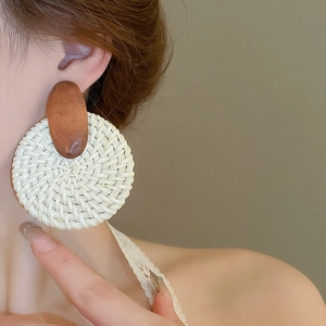 Détail rapproché de boucles d'oreilles créoles en raphia avec clou ovale en bois brun