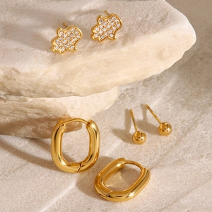 Detailliertes Set aus drei goldenen Ohrringen mit Hamsa-Hand-Steckern und ovalen Creolen