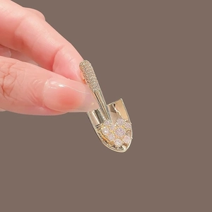 Detailed view of a gold shovel brooch with sparkling rhinestones being held by hand