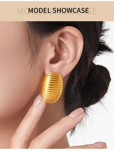Detail of large oval gold earring with textured linear ridges shown on a model