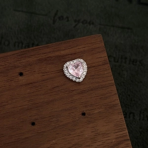 Macro shot of pink heart-shaped zircon stud earring on a dark wooden jewelry display stand