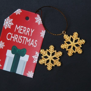 Close-up of glittery gold snowflake charms and red Merry Christmas gift tag on black background