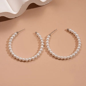 Macro shot of elegant circular pearl hoop earrings on a warm brown minimalist background