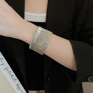 Close-up of wide silver metal cuff bracelet featuring a textured linear brushed finish