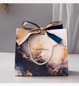 Detail of royal blue marble gift bag with blue gold ribbon bow and woven handles
