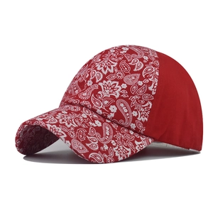 Detailed side view of red baseball cap with white paisley print on the curved brim and crown