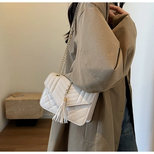 Close-up of cream quilted chain strap bag with tassel detail worn with a trench coat