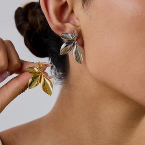 Detail showing 18k gold and silver leaf-shaped stainless steel earrings on model