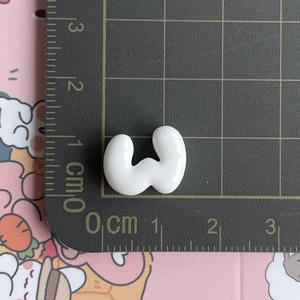 Macro detail of a 1.5cm white resin letter W charm on a measurement grid mat