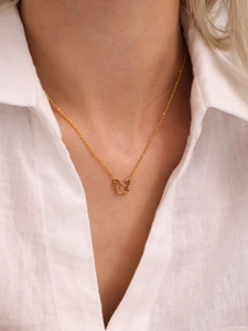 Close-up of gold butterfly necklace with colorful stones worn by a model in white shirt