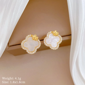 Detailed macro view of gold clover earrings with white shell and sparkling crystal inlay