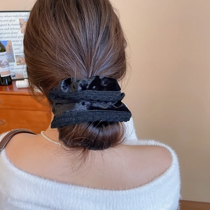 Detailed view of a black velvet scrunchie styled on a classic high bun hairstyle