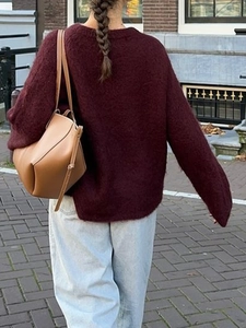 Women's burgundy knit sweater and jeans styled with a leather shoulder bag street view