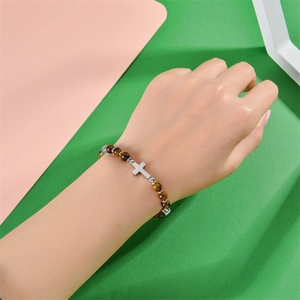 Bracelet en perles œil de tigre brun avec breloque croix en argent porté au poignet