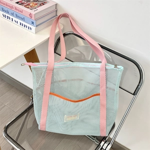 Détail du sac de plage en maille bleu clair avec anses roses et poche orange sur chaise