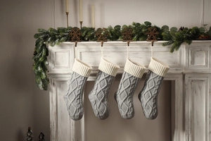 Detail of four grey knitted Christmas stockings with diamond pattern hanging on a white fireplace