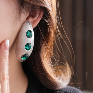 Close-up of matte silver oval earrings with three green gemstones worn by a model