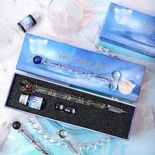 Close-up of a glass dip pen set with ink and holder in a blue starry sky gift box