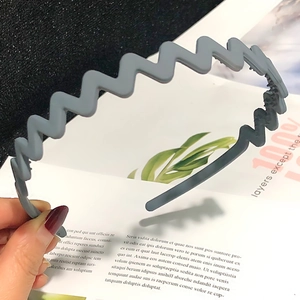 Close-up of a wavy grey candy-colored headband held by hand with a stylish magazine background