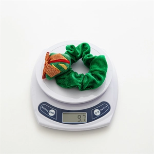 Detailed weight measurement showing a green velvet Christmas scrunchie at 9.7g on a scale